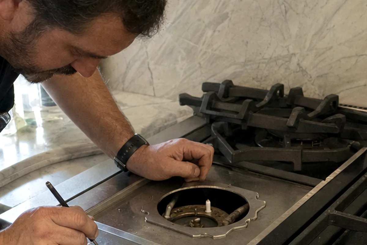 A rangetop with its grates removed, one burner well open and a probe laid across the stainless deck